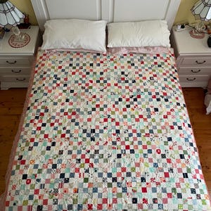 May include: A patchwork quilt featuring a grid of small, multi-colored fabric squares in various patterns including stripes, florals, and solid colors. The quilt displays a repeating design of red, blue, green, pink, and white tones throughout.