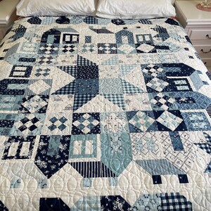 May include: A white quilt with a blue and white patchwork design. The quilt is made up of various geometric shapes and patterns, including squares, diamonds, and stars. The quilt is quilted with a simple stitch pattern.