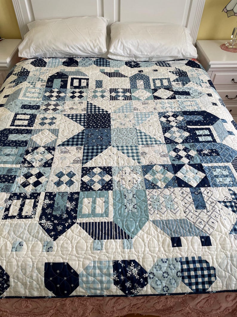 May include: A white quilt with a blue and white patchwork design. The quilt is made up of various geometric shapes and patterns, including squares, diamonds, and stars. The quilt is quilted with a simple stitch pattern.