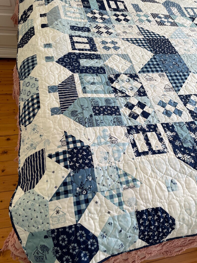 May include: A white quilt with a blue and white patchwork design. The quilt is made up of various geometric shapes and patterns, including squares, triangles, and circles. The quilt is quilted with a wavy pattern.