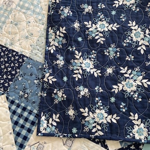 May include: A blue and white quilt with a floral pattern. The quilt is made of different fabrics and has a quilted design.