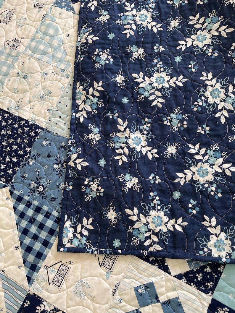 May include: A blue and white quilt with a floral pattern. The quilt is made of different fabrics and has a quilted design.