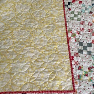 May include: A yellow and white quilt with a red binding. The quilt is quilted with a pattern of curved lines. The back of the quilt is made of patchwork squares in various colors and patterns.