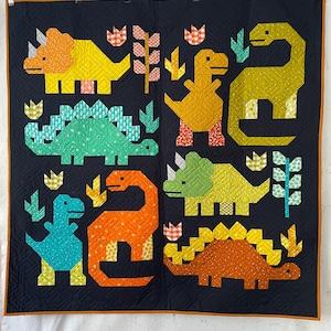 May include: A handmade quilt featuring colorful dinosaur designs on a navy blue background. The quilt showcases various dinosaurs in shades of yellow, green, orange, and blue, with decorative floral and leaf accents. The quilt is bordered with an orange trim.