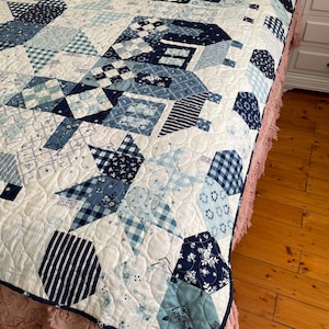 May include: A white quilt with a blue and white patchwork design. The quilt is made up of various geometric shapes, including squares, triangles, and hexagons. The quilt is edged with a blue trim.