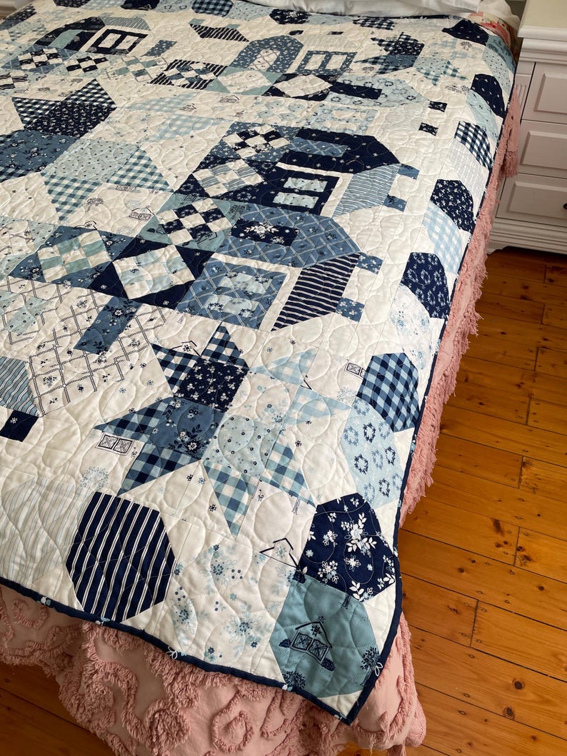 May include: A white quilt with a blue and white patchwork design. The quilt is made up of various geometric shapes, including squares, triangles, and hexagons. The quilt is edged with a blue trim.