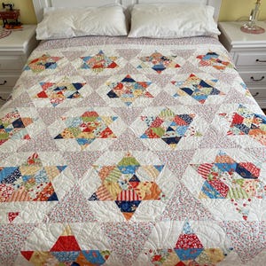 Op de afbeelding: Een wit dekbed met een patchwork-ontwerp met verschillende kleurrijke bloemenpatronen. Het dekbed ligt op een wit bed met twee witte kussens.