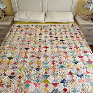 May include: A patchwork quilt featuring a repeating pattern of triangles and squares in a multitude of colours and small-scale prints. The quilt is stitched with a swirling, continuous line quilting design and covers a bed with two white pillows.