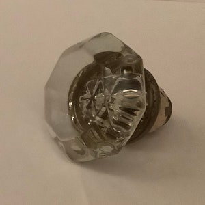 May include: A clear glass door knob with a faceted design. The knob has a metal base.