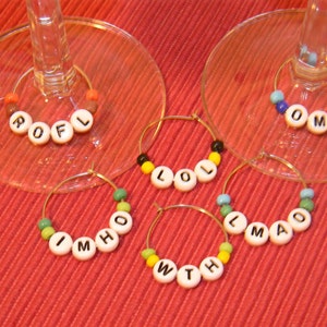 May include: Five glass wine charms with colorful beaded letters spelling out "ROFL", "LOL", "IMHO", "WITH", and "LMAO".