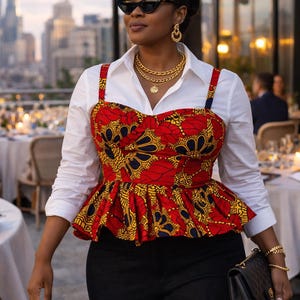 May include: A woman wearing a white collared shirt with a red, yellow, and blue patterned bustier top and black pants. She is wearing sunglasses, gold jewelry, and carrying a black purse. The background shows a city skyline.