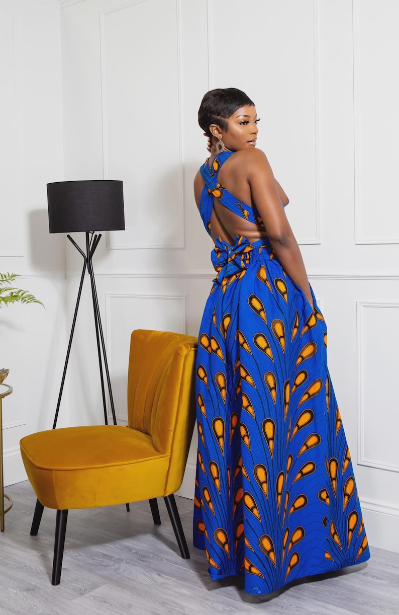 May include: A floor-length blue dress featuring a vibrant orange and black peacock feather-inspired pattern. The garment has a sleeveless bodice with a crisscross back design, a tie-waist detail, and a full, flowing skirt with side pockets.