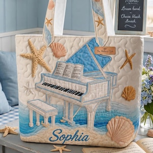 May include: Cream tote bag with a beach theme, featuring a piano, seashells, and starfish appliqués. The bag has a blue and white colour scheme, with the name "Sophia" embroidered on the front. The handles are white with seashell accents.