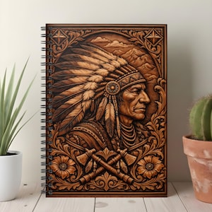 May include: A spiral-bound notebook with a detailed, carved wooden cover. The cover features a portrait of a Native American chief in profile, wearing a feathered headdress. Intricate floral and geometric patterns surround the central image, with crossed tomahawks at the bottom.