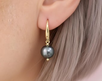 May include: A gold-colored earring with a dark gray pearl. The earring is a drop style, with a curved hook that attaches to the ear. The pearl is round and has a smooth surface. The earring is shown on a person's ear.