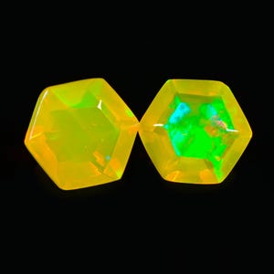 Peut inclure: Deux pierres précieuses hexagonales et facettées d'une couleur jaune-orangé vibrante. Les gemmes ont un aspect brillant, presque incandescent, avec des éclairs internes de vert et de bleu. Le fond est noir uni, soulignant l'éclat des gemmes.