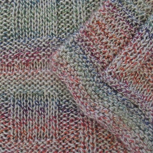 May include: Close-up of a knitted fabric with a multi-colored yarn. The fabric has a textured pattern with a mix of white, red, blue, green, and purple threads.