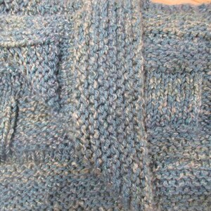 May include: Close-up of a knitted fabric with a blue and white color scheme. The fabric has a textured pattern with a variety of stitches.