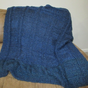 May include: A blue knitted throw blanket with a textured pattern. The blanket is folded and draped over a brown couch.