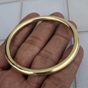 以下が含まれることがあります： 金色の円形バングルブレスレット。ブレスレットは、滑らかで光沢のある表面を持つ、金属製のソリッドバンドです。バングルは手で持たれており、その丸い形と金属的な輝きを際立たせています。ブレスレットはシンプルでエレガントなジュエリーです。