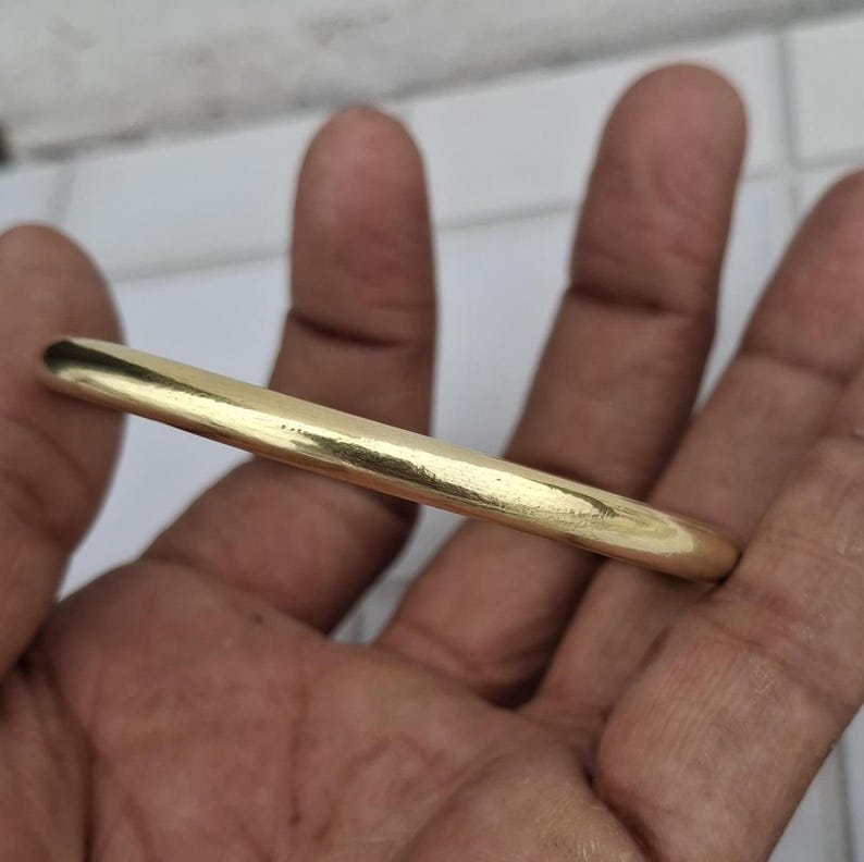 以下が含まれることがあります： ゴールドカラーのバングルブレスレット。滑らかで丸みを帯びたブレスレットは、光を反射する研磨仕上げです。このジュエリーは、シンプルでエレガントなデザインで、日常使いに適しています。バングルの直径は約0.64cmです。