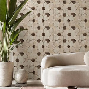 May include: A modern living room with a beige sofa, round coffee table, and a patterned wall. A large potted plant and a pink rug add color. Decorative items include a sphere and a vase.