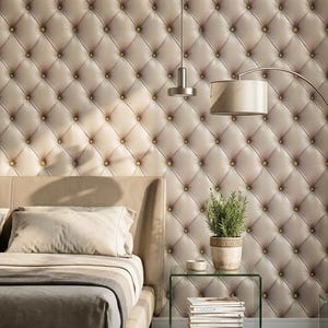Puede incluir: Un dormitorio con cabecero y pared tapizados. La pared es de color beige claro con un patrón de diamantes y botones dorados. Una cama con estructura de cuero marrón, almohadas y una manta está en primer plano. Una mesita de noche de cristal con una planta y libros está al lado de la cama.