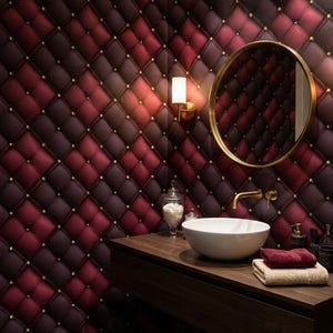 Könnte beinhalten: Luxuriöses Badezimmer-Interieur mit einer gesteppten bordeauxroten und dunkelroten Wand mit goldenen Akzenten. Ein runder goldener Spiegel hängt über einem dunklen Holzwaschtisch mit einem weißen Waschbecken, Handtüchern und Accessoires.