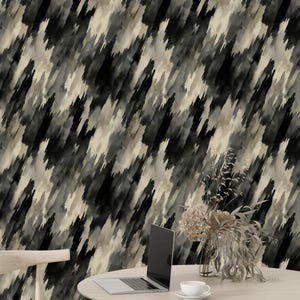 Puede incluir: Escena interior moderna con una mesa redonda de madera con un portátil, una taza de café y un jarrón con flores secas. El fondo es una pared con un patrón abstracto negro, gris y beige. Una silla de madera a la izquierda.