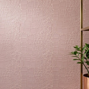 May include: A light pink wallpaper featuring a raised, embossed texture that mimics the appearance of crocodile skin. The surface has a repeating pattern of irregular, rectangular scales with deep grooves, creating a tactile, three-dimensional effect.