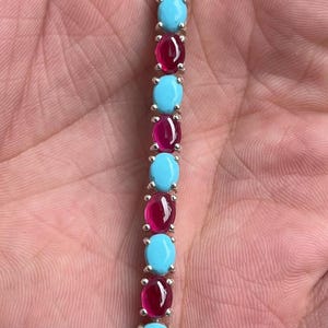 Peut inclure: Un bracelet aux tons argentés présentant un motif alterné de pierres ovales bleu clair opaques et de pierres ovales rouge foncé translucides. Chaque pierre est sertie individuellement dans une monture en métal à griffes.