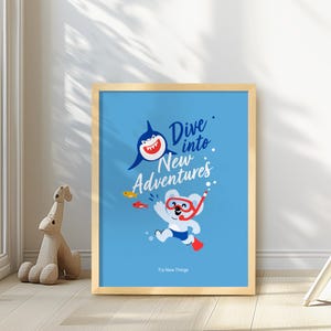 May include: A framed art print with a light wood frame. The print features a cartoon shark and a koala bear wearing a snorkel, with the words "Dive into New Adventures" and "Try New Things" on a blue background.