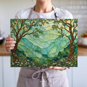 May include: A rectangular decorative panel featuring a stained-glass style landscape with two trees and a mountain range. The artwork uses shades of green, blue, and yellow. White flowers are at the base of the trees. The panel is held by a person.