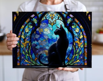 Peut inclure: Une œuvre d'art encadrée représentant un chat noir devant une fenêtre en vitrail. La fenêtre présente des bleus, des verts, des jaunes et des violets. L'œuvre est tenue par une personne portant une chemise blanche et un tablier gris.