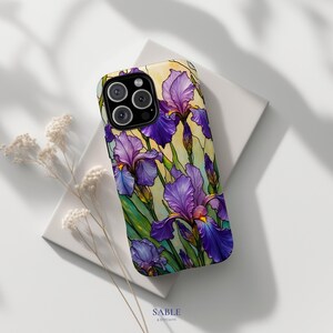May include: A phone case featuring a stained-glass style design of purple irises with green leaves and yellow background. The case has a black camera module and the text "SABLE & STITCH CO." at the bottom.