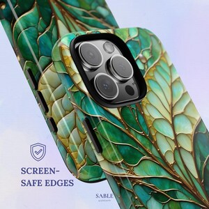 May include: A close-up of two phone cases with a leaf design in shades of green and gold. The cases have a glossy finish and a black camera frame. The text "SCREEN-SAFE EDGES" is visible on the left side of the image.