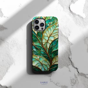 May include: A smartphone case with a leaf design. The case features a pattern of green and gold leaves with a textured appearance. The case has a glossy finish and is set against a white background. The brand name "SABLE & STITCH CO" is printed at the bottom.