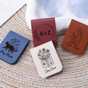 Könnte beinhalten: Eine Sammlung personalisierter Leder-Lesezeichen in verschiedenen Farben. Designs umfassen eine Katze mit Büchern, Blumenarrangements, Initialen und eine lesende Frau. Jedes Lesezeichen hat einen Namen.