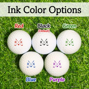 K&ouml;nnte beinhalten: Wei&szlig;e Golfb&auml;lle mit individuellen Tintenfarboptionen: Rot, Schwarz (Standard), Gr&uuml;n, Blau und Lila. Jeder Ball zeigt die Initialen "R" und "K" mit einem Golfschl&auml;ger- und Ball-Design. Der Text "Tintenfarboptionen" steht oben.