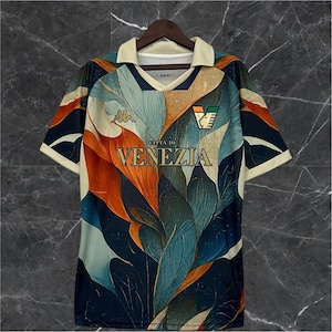 May include: A short-sleeve jersey featuring a cream-colored collar and a vibrant abstract leaf pattern in shades of dark blue, orange, and light teal. The chest displays the text CITTA DI VENEZIA in gold lettering, a Kappa logo, and a stylized crest.