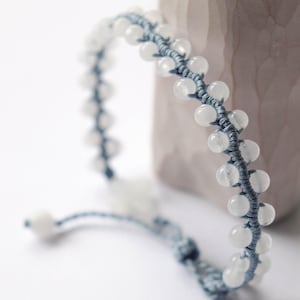 May include: A handmade bracelet featuring a series of white, round beads strung together with a blue cord. The bracelet is displayed on a white surface, with a blurred background. The beads are approximately 0.3 inches in diameter.