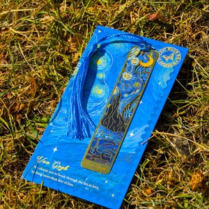 Puede incluir: Un marcap&aacute;ginas azul con la pintura "La noche estrellada" de Van Gogh, con un marcap&aacute;ginas de metal dorado. El marcap&aacute;ginas tiene una borla azul y el texto "East River PO 2.5 Avenue D". El texto "Van Gogh" y una cita tambi&eacute;n son visibles.
