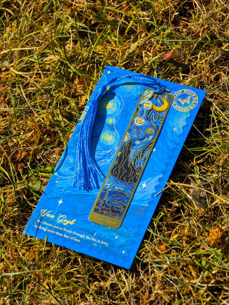 Puede incluir: Un marcap&aacute;ginas azul con la pintura "La noche estrellada" de Van Gogh, con un marcap&aacute;ginas de metal dorado. El marcap&aacute;ginas tiene una borla azul y el texto "East River PO 2.5 Avenue D". El texto "Van Gogh" y una cita tambi&eacute;n son visibles.