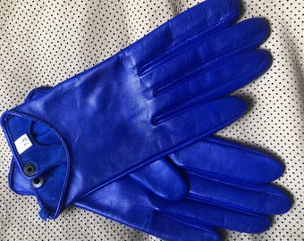 May include: A pair of vibrant blue leather gloves. The gloves are a bright, solid blue color and appear to be made of smooth leather. A small white tag with the number "7.5" is visible on the wrist of one glove. The gloves are likely for driving or fashion.