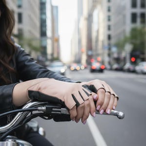Könnte beinhalten: Hellbraune, fingerlose Lederhandschuhe mit schwarzen Akzenten. Die Handschuhe sind für Motorradfahrer konzipiert. Das Bild zeigt die Handschuhe an einem Motorradlenker, mit einer Stadtstraße und Verkehr im Hintergrund.