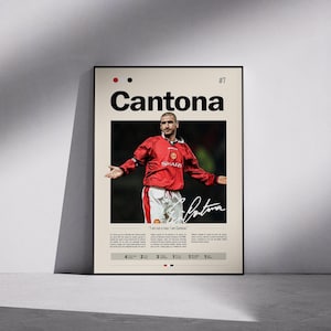 May include: A framed poster featuring a photograph of a soccer player in a red jersey and white shorts. The poster includes the name "Cantona" in bold black letters, the number "7", and the player's signature. The text "I am not a man. I am Cantona" is also visible.
