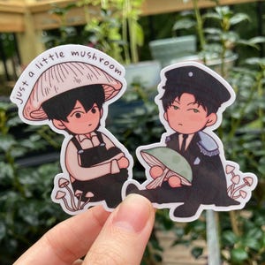 May include: Two stickers featuring cartoon characters with mushroom-themed designs. One sticker shows a character wearing a mushroom hat with the text "just a little mushroom". The other character is wearing a black uniform and holding a mushroom.