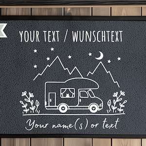 Puede incluir: Felpudo gris real con borde negro. El felpudo presenta una ilustraci&oacute;n blanca de una autocaravana, monta&ntilde;as, estrellas y una luna creciente. El texto dice "YOUR TEXT / WUNSCHTEXT" y "Your name(s) or text".