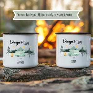 May include: Two white enamel camping mugs with black rims and handles. Each mug features a green camper illustration, trees, and the text "Camper TASSE". One mug says "VON ANDRE" and the other says "VON SINA". The background shows a campfire.