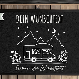 Puede incluir: Felpudo rectangular negro con una ilustraci&oacute;n blanca de una autocaravana, monta&ntilde;as, estrellas y luna. El texto "DEIN WUNSCHTEXT" est&aacute; en la parte superior y "Namen oder Wunschtext" en la inferior. La palabra "BLACK" est&aacute; en una pancarta blanca en la esquina superior izquierda.